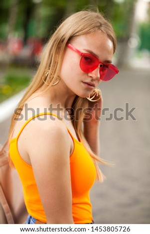 Close up portrait of a pretty young blonde schoolgirl in orange t-shirt, summer park outdoor