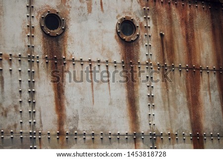RUST AND TEXTURE ON METAL PLATE SIDES OF STAGED SHIPWRECK WITH RIVETS AND PORTHOLES
