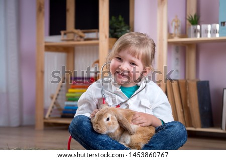 Child playing veterinarian doctor with rabbit. Happy smiling kid girl at home or daycare. Pediatrician. Preschool, school and kindergarten kids take care about animal. Pediatric, healthcare 