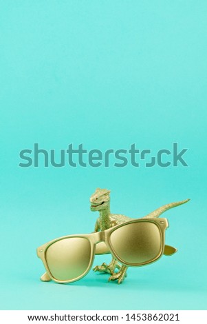 Golden dinosaur toy holding golden sunglasses. Summer trends, fashion, sales, shopping concept