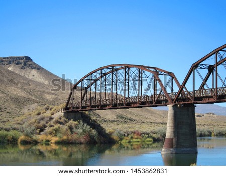 Steel truss railroad bridge over the Snake River in Idaho with foothills in the background and a blue sky.