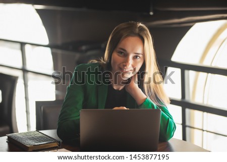 Beautiful woman with long hair in a green jacket sitting at a laptop and smiling.