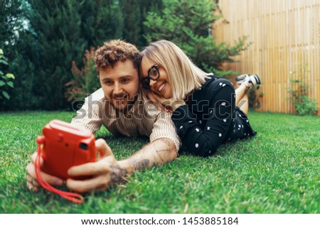 Young couple in love taking a selfie with an instant camera. Lying on the grass in the yard of his house