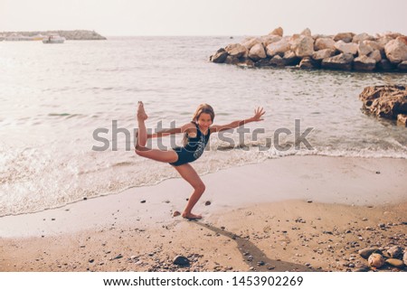 Little girl having fun at tropical beach during summer vacation playing together at shallow water. Cute kid making sporty exercises on the seashore