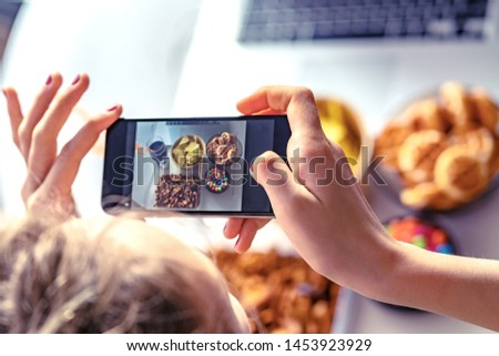 Girl eats fast food and take a pictures of it on smartphone at work. Unhealthy food: chips, crackers, candy, waffles, cola. Junk food, concept.