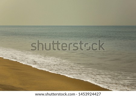 yellow sandy beach against the backdrop of a calm ocean with foamy waves under a clear sky