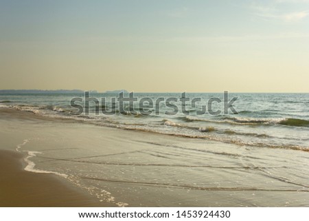 yellow sandy beach against the backdrop of the foam of the ocean waves under a clear sky