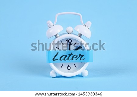 Procrastination, delay and urgency concept. White alarm clock with a sticky note with text later. Royalty-Free Stock Photo #1453930346
