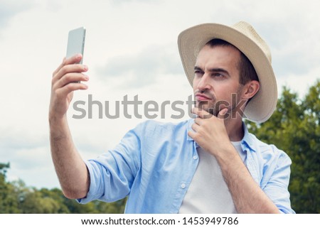 Selfie of narcissistic man in hat, attractive man uses a mobile phone outdoors, portrait, toned Royalty-Free Stock Photo #1453949786