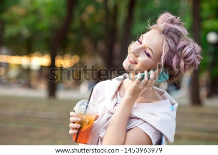 Happy cheerful young blonde with pink hair, walks against the backdrop of the city, calls on a mobile phone to his friends. Blonde student is resting on the street after college to meet friends.