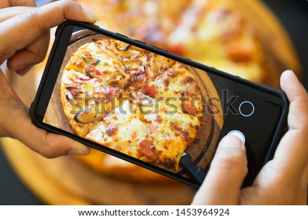 Food blogger taking picture of cooked pizza. Woman's hands with smartphone takes picture of fresh baked hot selfmade pizza.  Photography blogging workshop concept.