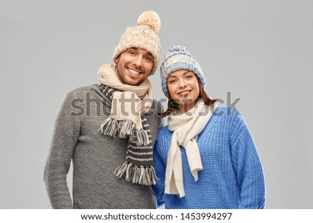 people, christmas and winter clothes concept - happy couple in knitted hats and scarves over grey background