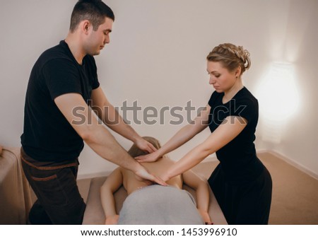 two masseurs do four hands massage in the spa for a young woman, professional massage.