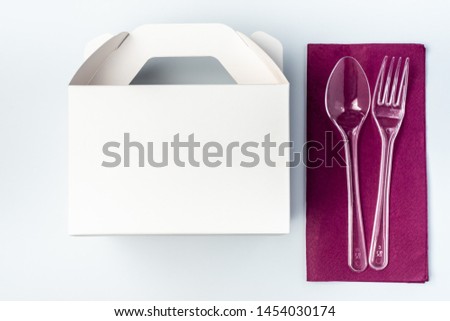 White Cardboard Fast Food Box, Packaging For Lunch and plastic fork and spoon on purple serviette. On White Background Isolated. Ready For Your business design