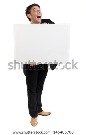 Businessman holding a blank white card or sign in front of his chest with an exaggerated open-mouthed look of amazement, humorous portrait isolated on white