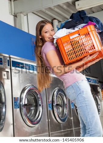Portrait of beautiful young woman carrying basket of clothes in laundry