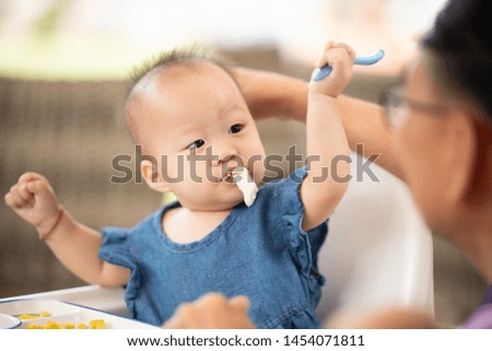 Grandfather feeding her baby girl with a spoon.First solid food for young kid.Baby weaning.Healthy nutrition for children. Parents feed kids.