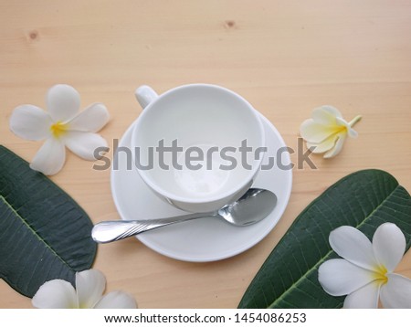 Blank white cup with frangipani flowers and jug on wooden table