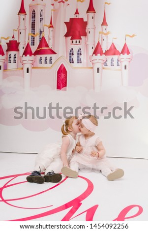 Portrait of a little girls, luxury princess in dress on background pink castle. Concept of birthday celebration is 1 year. A childs, kids sitting on the floor and playing.