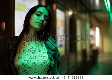 Beautiful girl street portrait. Green Neon light, she's wearing an alien shirt.