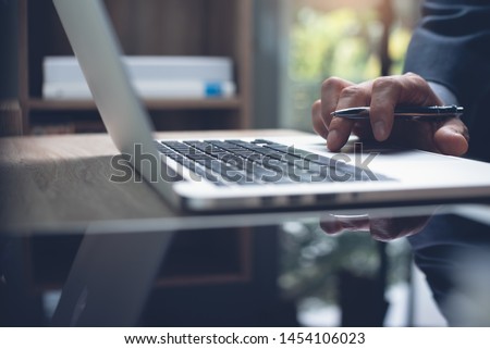 Business man typing on laptop computer keyboard with digital tablet on wooden desk, close up. Executive manager working laptop searching internet in modern office. Business and technology concept