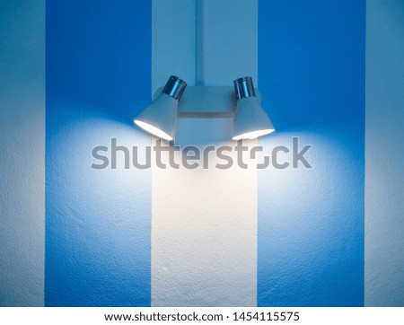 Wall lamp on white and blue striped wall background with copy space.