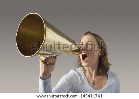 Angry businesswoman shouting through megaphone against gray background
