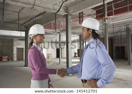 Side view of a woman and man shaking hands at construction site
