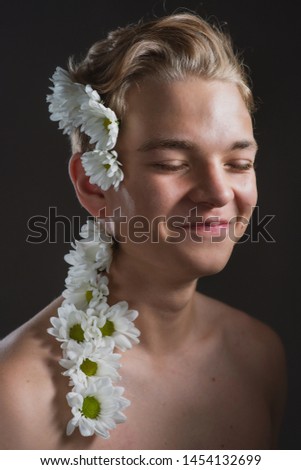 young handsome guy with flowers in her hair, beauty portrait of a young man with brown hair and bare torso, daisies in the hair of a man