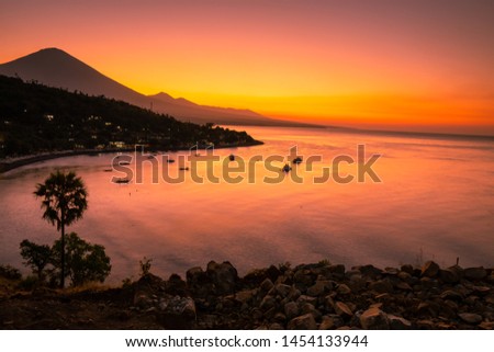 Sunset at Amed, Bali with boats and yachts anchored in shallow sea and mount Agung in background