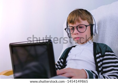 Boy in glasses and earphones is writing on laptop. Online study and learning