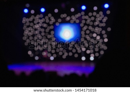 Blurred entertainment show backdrop. Sparkling stage lights. Ultra violet light beams spotlights and glowing led screen on the stage. Silhouette shot from back. Small depth of view.