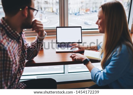 Male and female near blank laptop screen, cooperation of two ?aucasian skilled students installing new software and applications on netbook in cafe engage in e learning successfully write course work