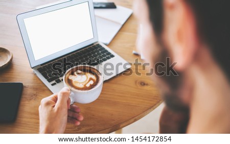 Cropped image of male programmer with coffee cup in hand watching online movie on website via application on modern laptop computer with copy space area for advertising text, blank screen netbook