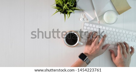 Top view of man typing on keyboard in minimal white work space with office supplies 