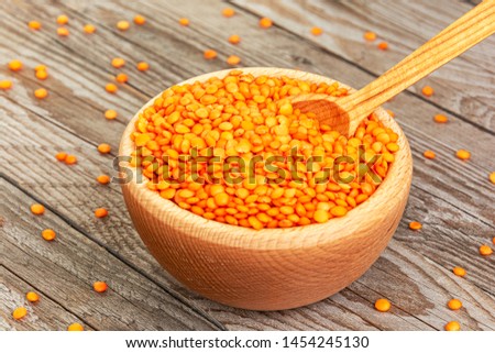 Photo of red lentils in wooden bowl with spoon on wooden background. Product photo of red lentils. Healthy lifestyle. Vegetarian and vegan diet. Spilled lens