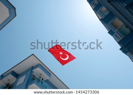 The Turkish red flag with the moon and star on a background of blue sky surrounded by buildings. Bottom view, the flag is inverted, fluttering in the wind. The concept symbols of the countries.