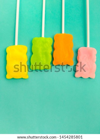 Close-up image of four colorful teddy bear shape lollipop candy on blue colored background with copy space.