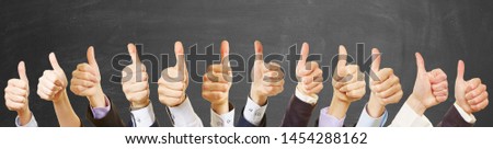 Business team with thumbs up in front of blackboard