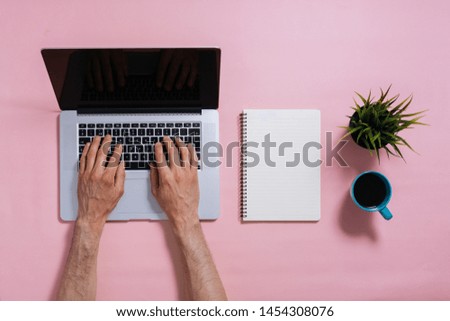 flat lay of male hands typing on laptop keyboard on pink background