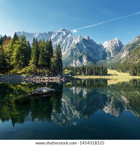 Idyllic landscape in the Alps with calm mountain lake and majestic Mangart mount under sunlight in summer. Amazing nature scenery with reflections. Fusine lake. Italy. postcard. picture of wild area