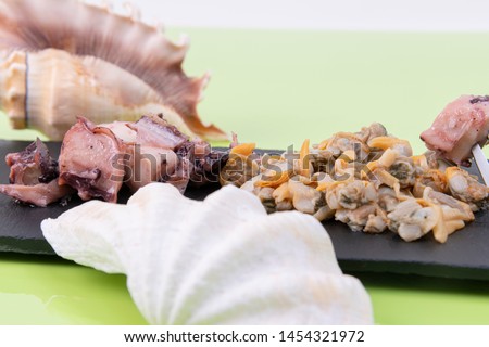 Close-up of tasty seafood, cockles served with pot?n on a black plate with sea shells decorating the photo on a green photo