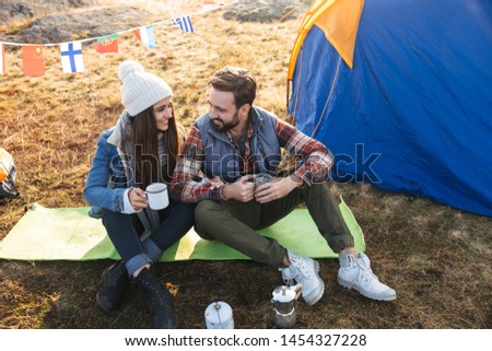 Photo of happy young loving couple outside with tent in free alternative vacation camping over mountains drinking hot tea.