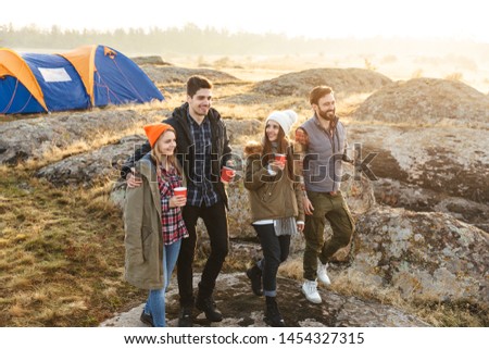 Photo of young group of friends outside in free alternative vacation camping over mountains drinking hot tea talking with each other.