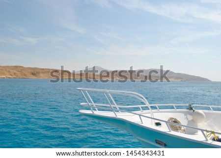 Part of the yacht against the blue sea, in the distance mountains and yellow sand. Royalty-Free Stock Photo #1454343431