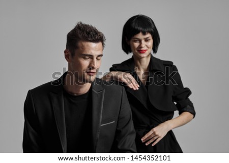 Extravagant Woman in a black coat with bright makeup leaned on the shoulder of a young man in a suit