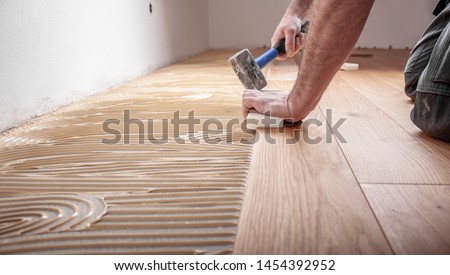 Craftsman lays parquet floor and spreads the glue on the screed and beats the floorboards with the hammer and the block Royalty-Free Stock Photo #1454392952