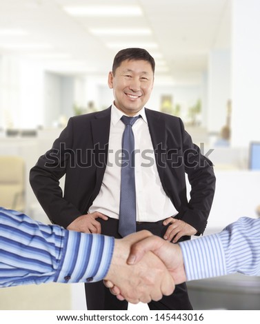 Business handshake between two colleagues on the background of happy asian businessman  