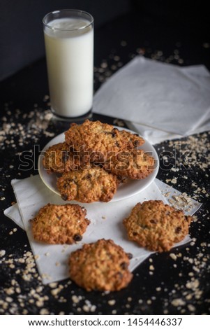 Oatmel cereal cookies wih glass of milk on a black background with white napkins and crunches on the black wooden table