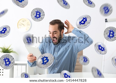 Emotional young man with tablet celebrating victory in office under bitcoin rain 